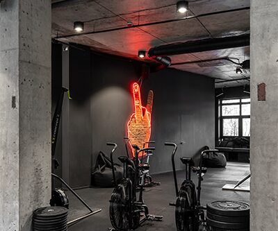 Неонова рука на чорній стіні і велотренажери в My F+ckin’ Gym