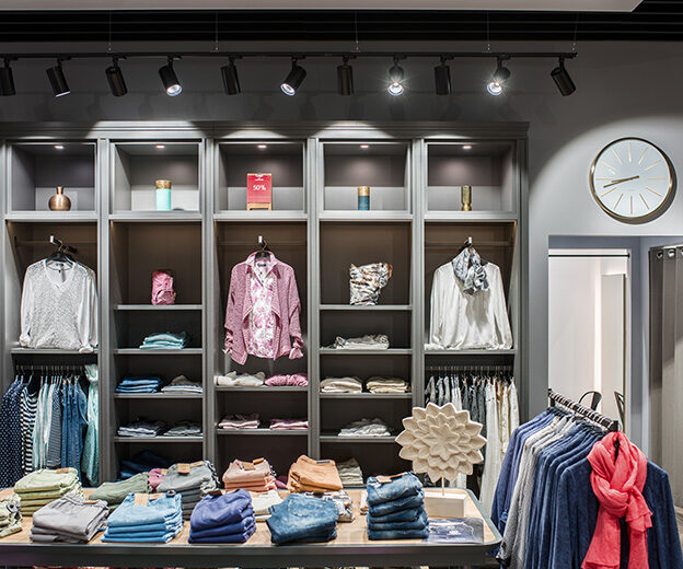 Womenswear shelving and a denim table in the LERROS shop under a line of track luminaires