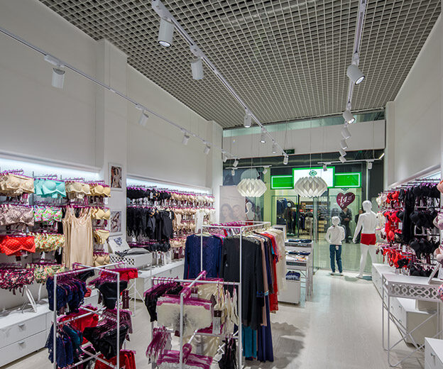 Проход в магазине Anabel Arto с трековыми прожекторами на белом шинопроводе под потолком-грильято