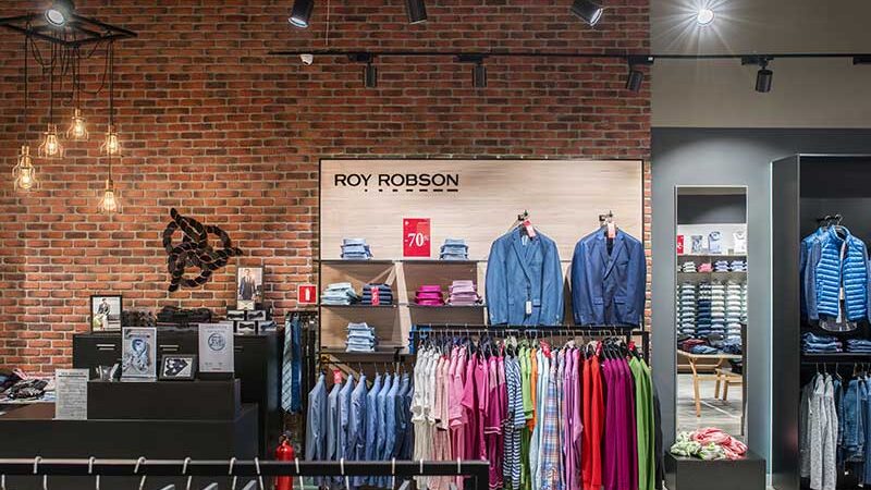 Кассовая зона и фирменная стена Roy Robson на фоне кирпичной стены, трековые светильники под потолком